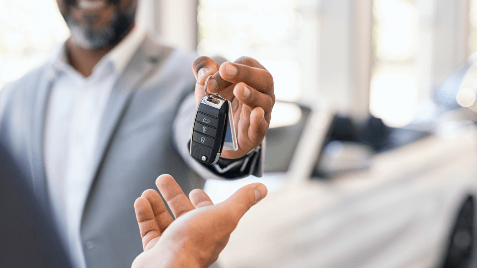 Man handing car keys to another person in dealership.