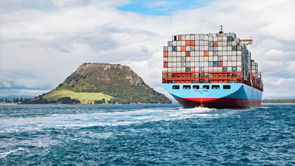 Large container ship sailing near a green coastal hill