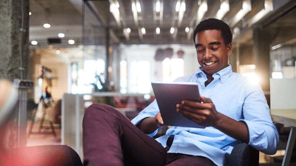 Man smiling while using a tablet in a modern office.