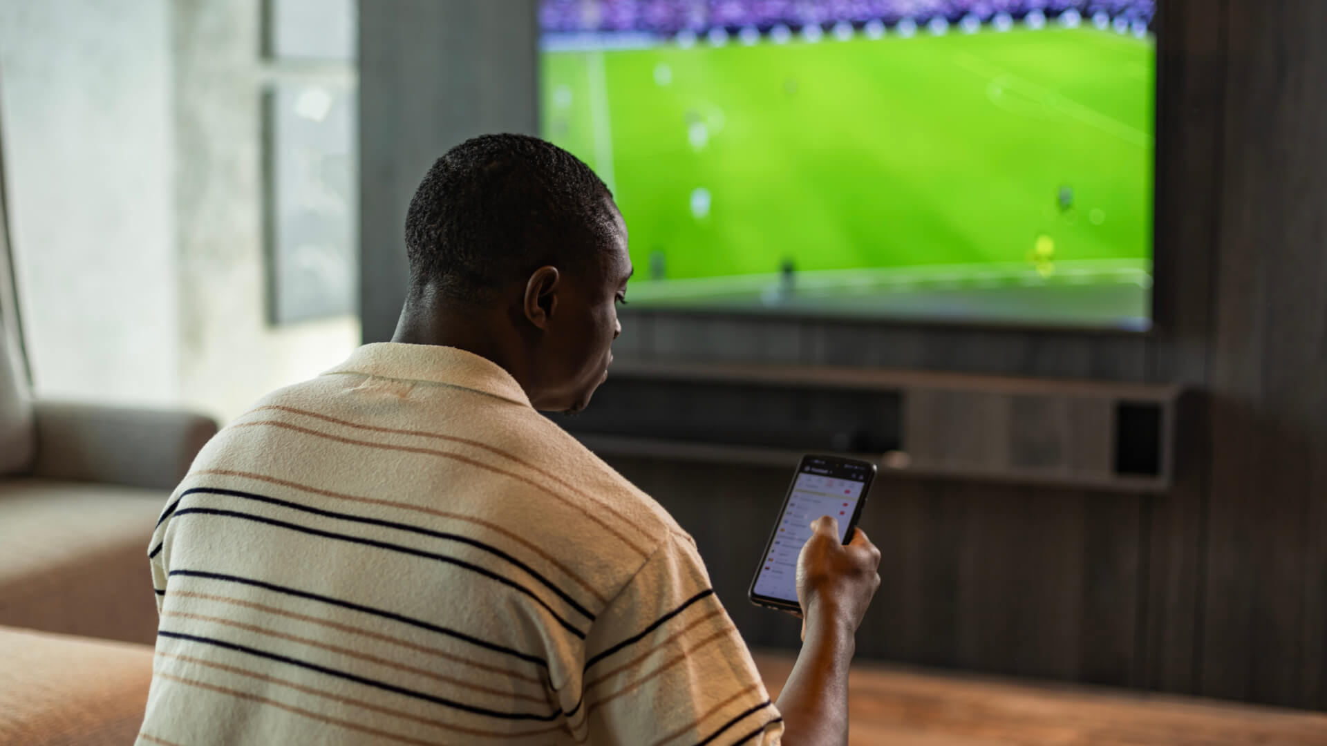 Man using a smartphone while watching soccer on TV.