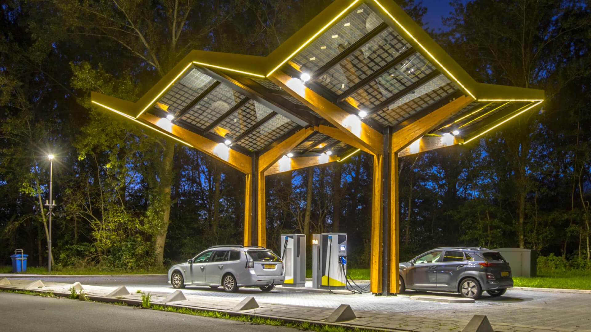 Two cars charging at an EV station under a lit canopy.