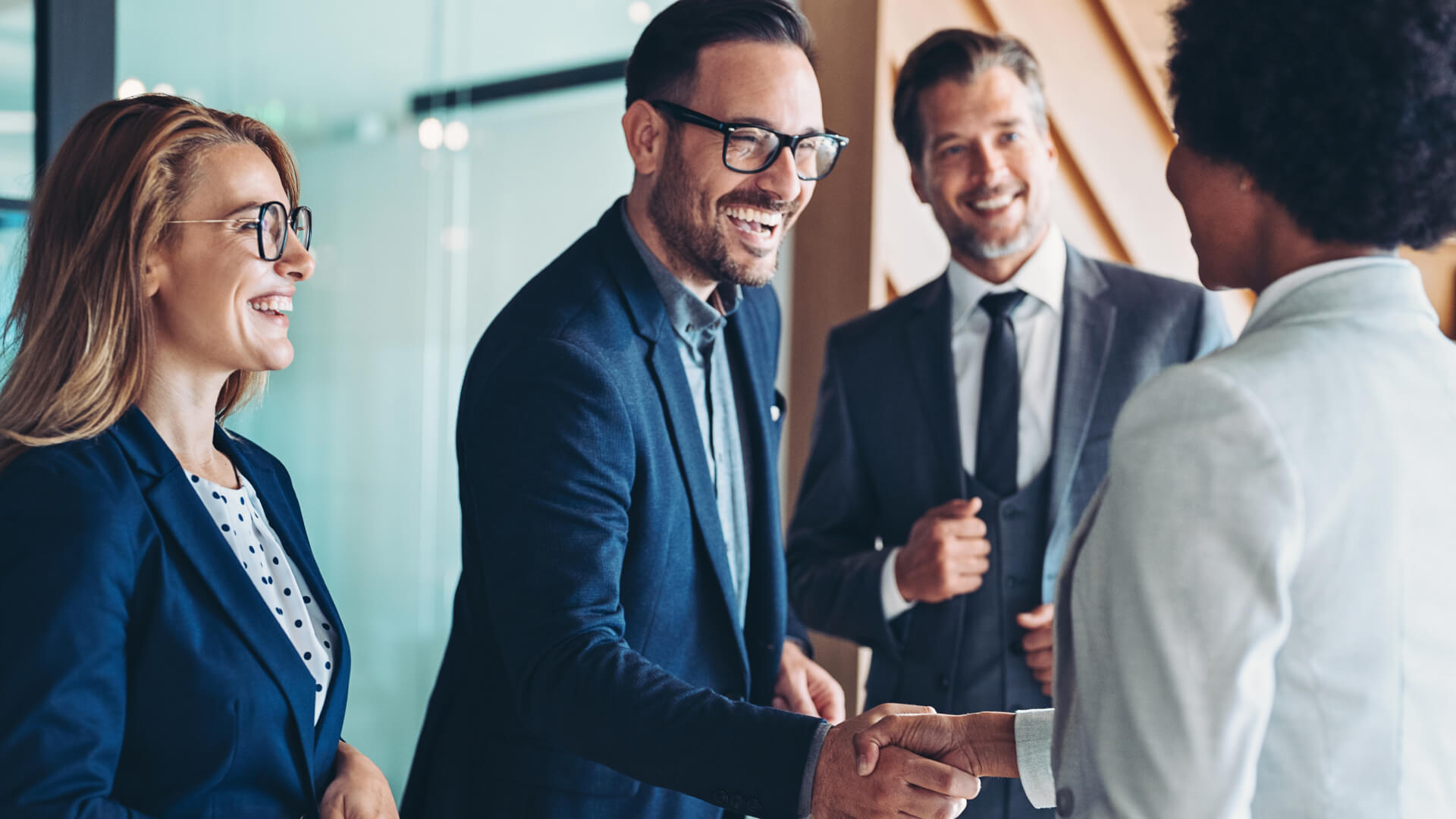 Professionals in suits smiling and shaking hands in office.
