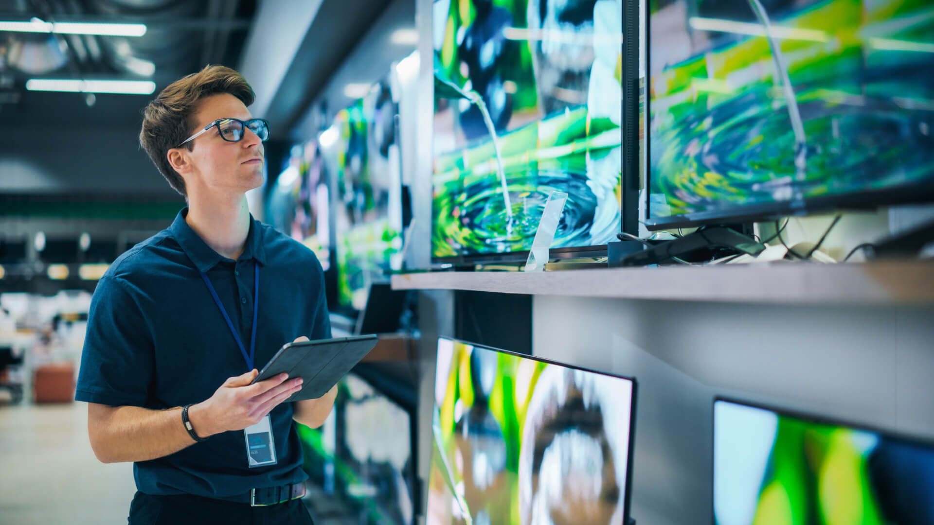 Person inspecting TVs in an electronics store aisle.