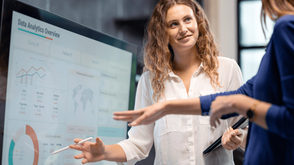 Two women discussing data analytics on a screen.