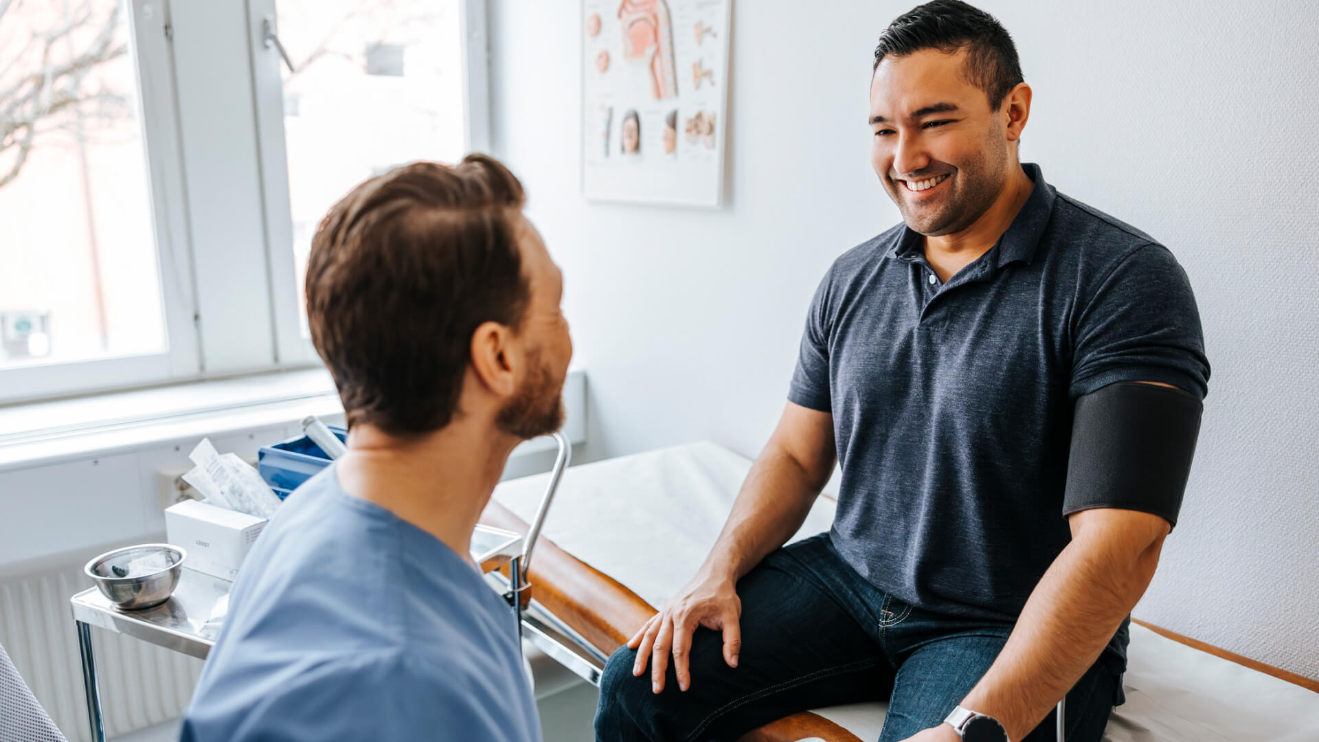 Doctor consulting a smiling patient wearing a blood pressure cuff.