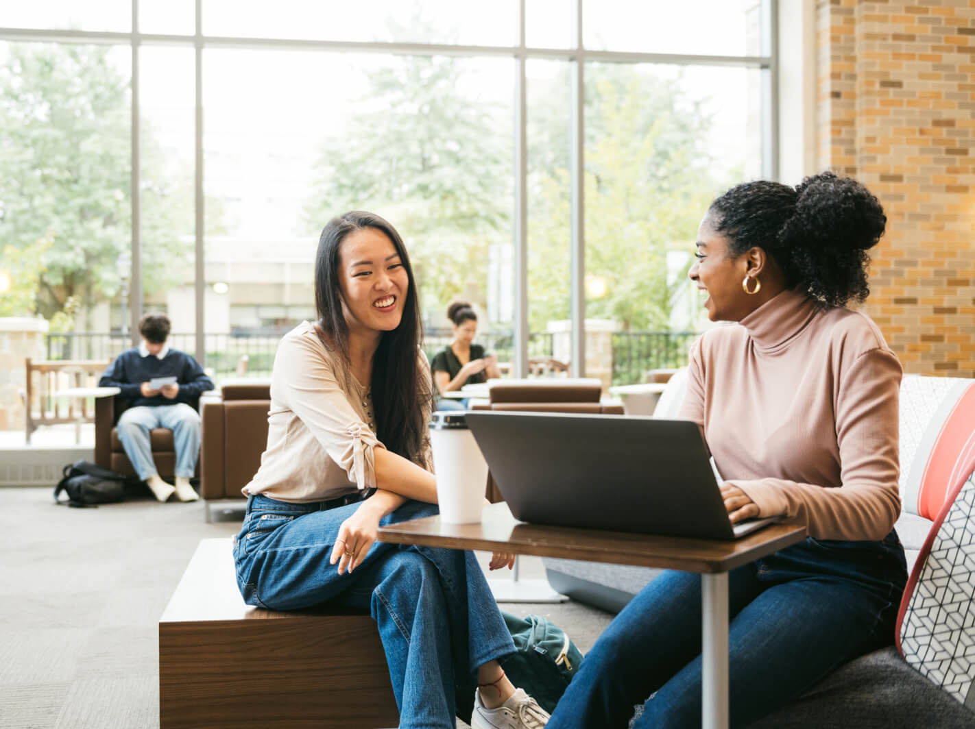Two women laughing together in a college lounge.