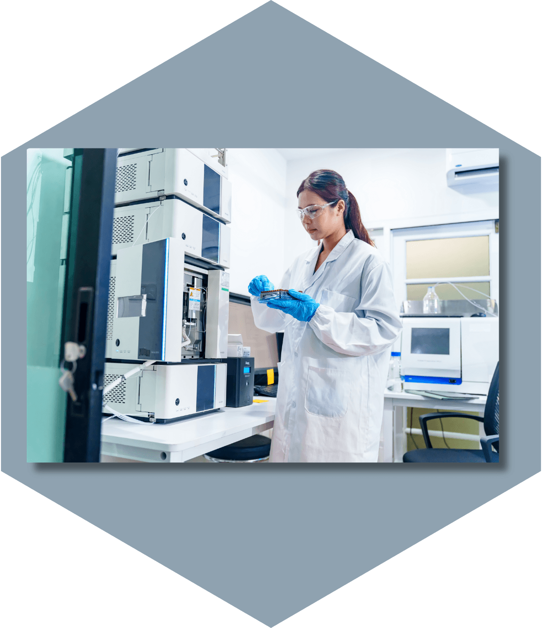 Person in lab coat examining petri dish in lab.