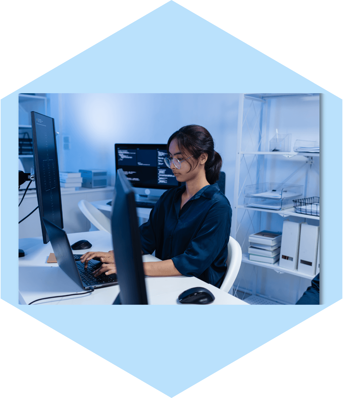 Woman coding on laptop with multiple monitors.
