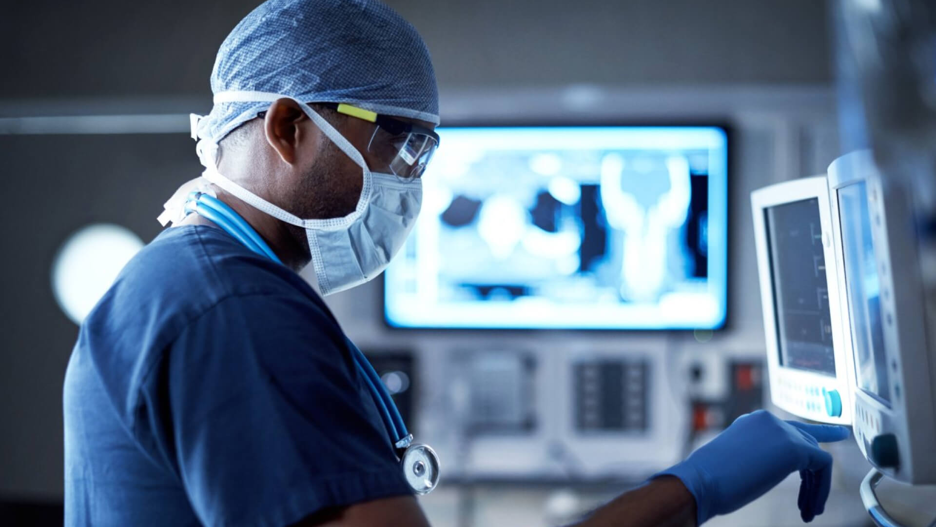 Doctor in PPE examining medical monitors.