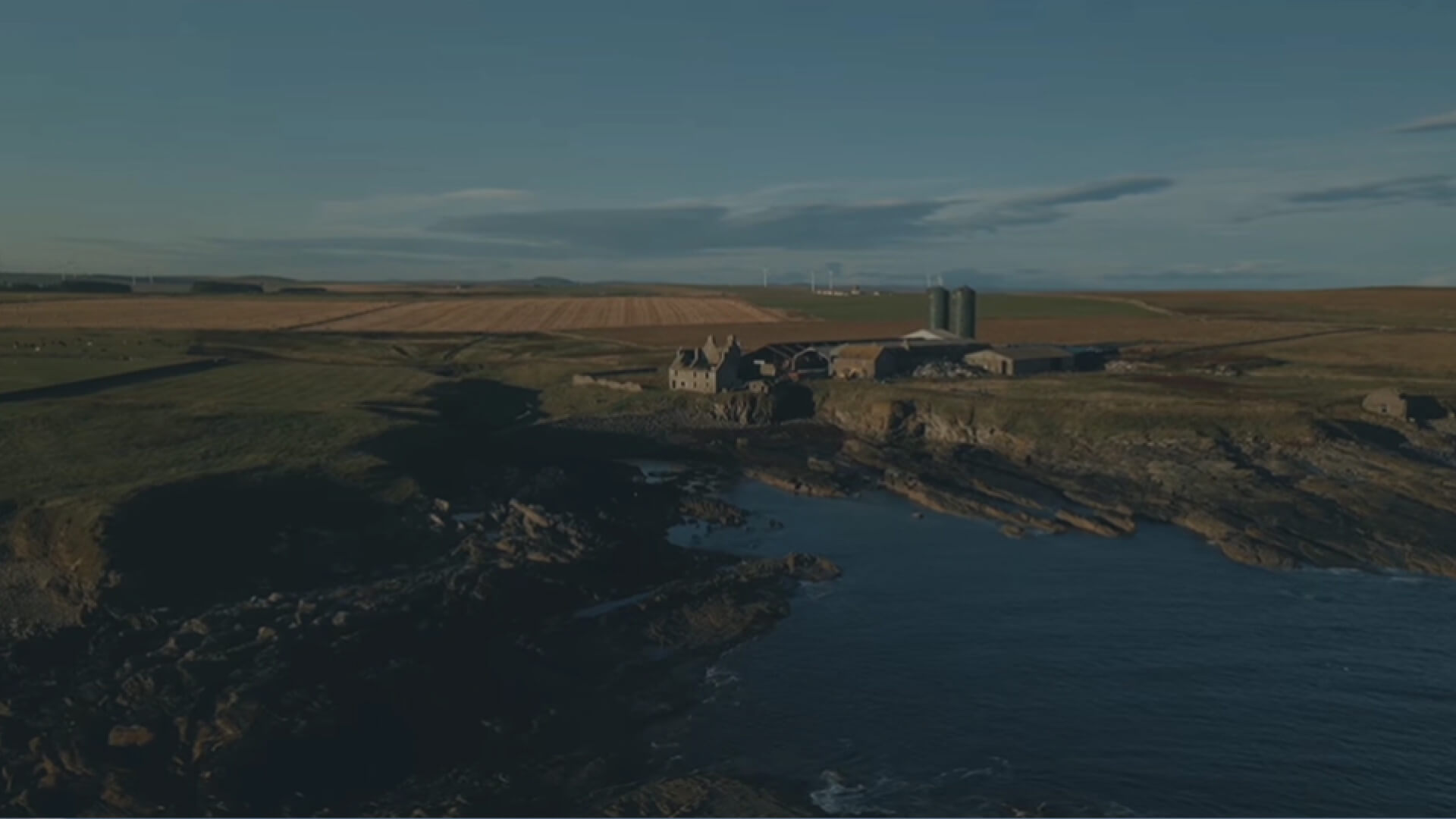 Coastal farm on cliffs, sea, fields, wind turbines.