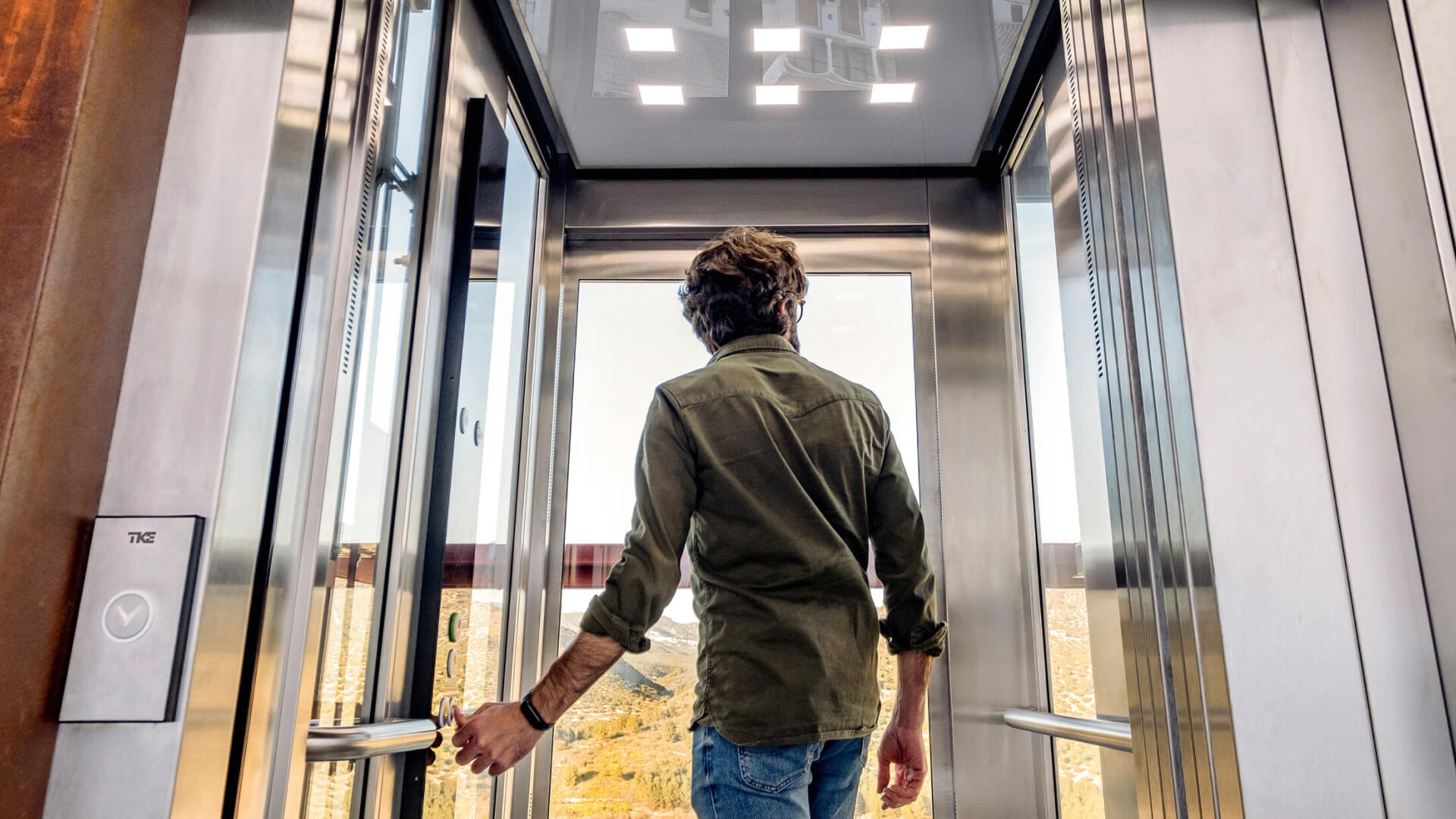 Man in glass elevator looking out at view.