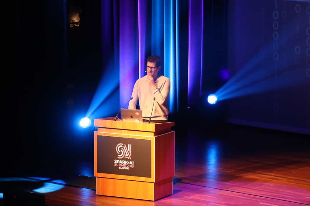 Oriol Vinyals speaks behind the podium onstage, which reads "Spark + AI Summit 2019 Europe."